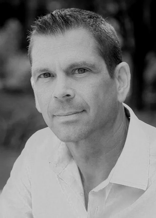 Black and white portrait of a man with short hair, wearing a white collared shirt, looking at the camera with a slight smile.