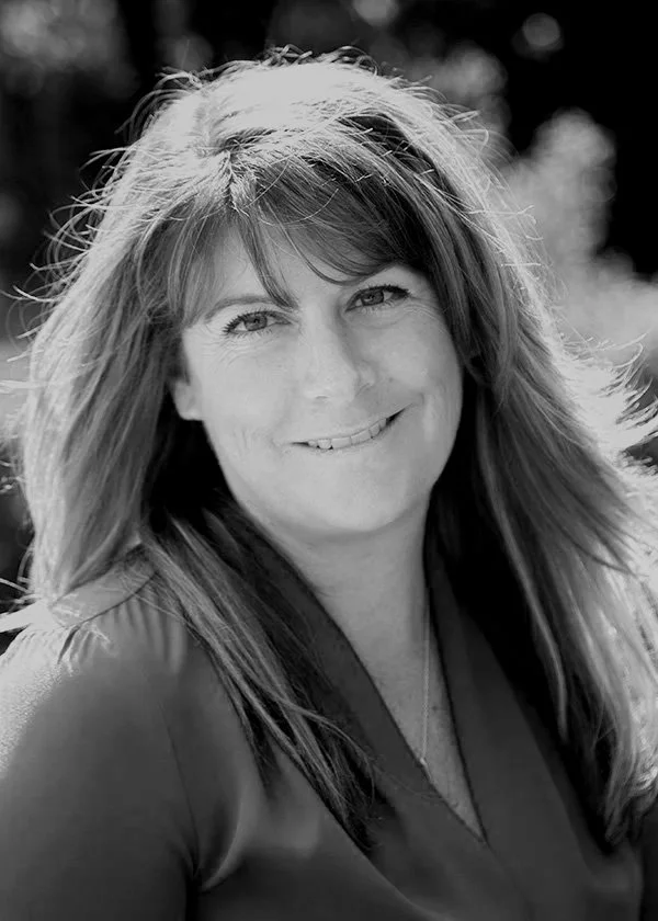 Black and white portrait of a smiling woman with long hair outdoors.