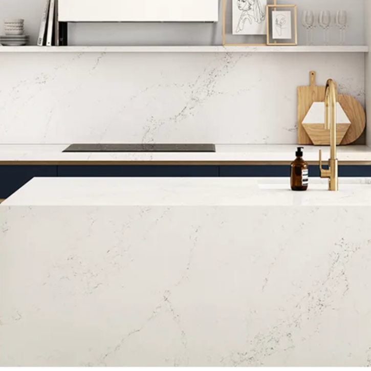 Modern kitchen with white marble countertops, a gold faucet, a soap dispenser, and decorative shelves with framed artwork and glassware.
