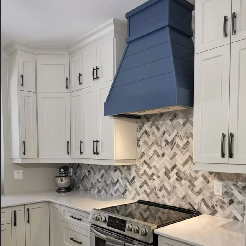 Kitchen with white cabinets, a blue range hood, marble backsplash, and a black cooktop.