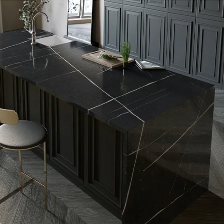 A modern kitchen island made of black marble with white veining, featuring a sink and a few decorative items on top, with gray cabinetry in the background.