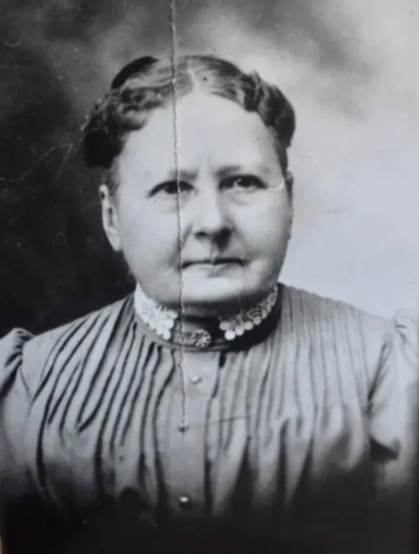 Black and white photograph of a woman with styled hair, wearing a striped shirt and a floral necklace, looking directly at the camera.