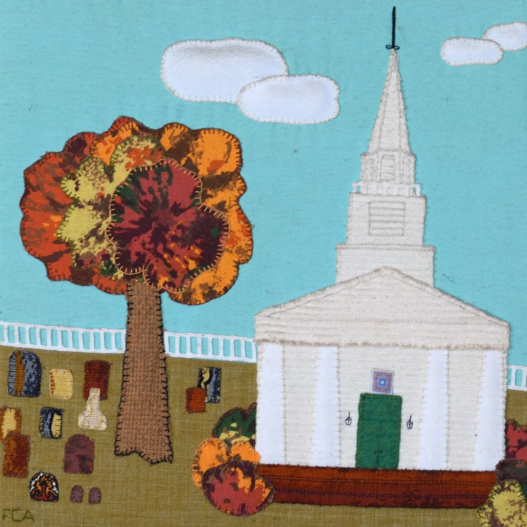 Embroidery artwork of a church with a tall steeple, a colorful autumn tree, a grassy area with small decorative objects, and a blue sky with a few clouds.