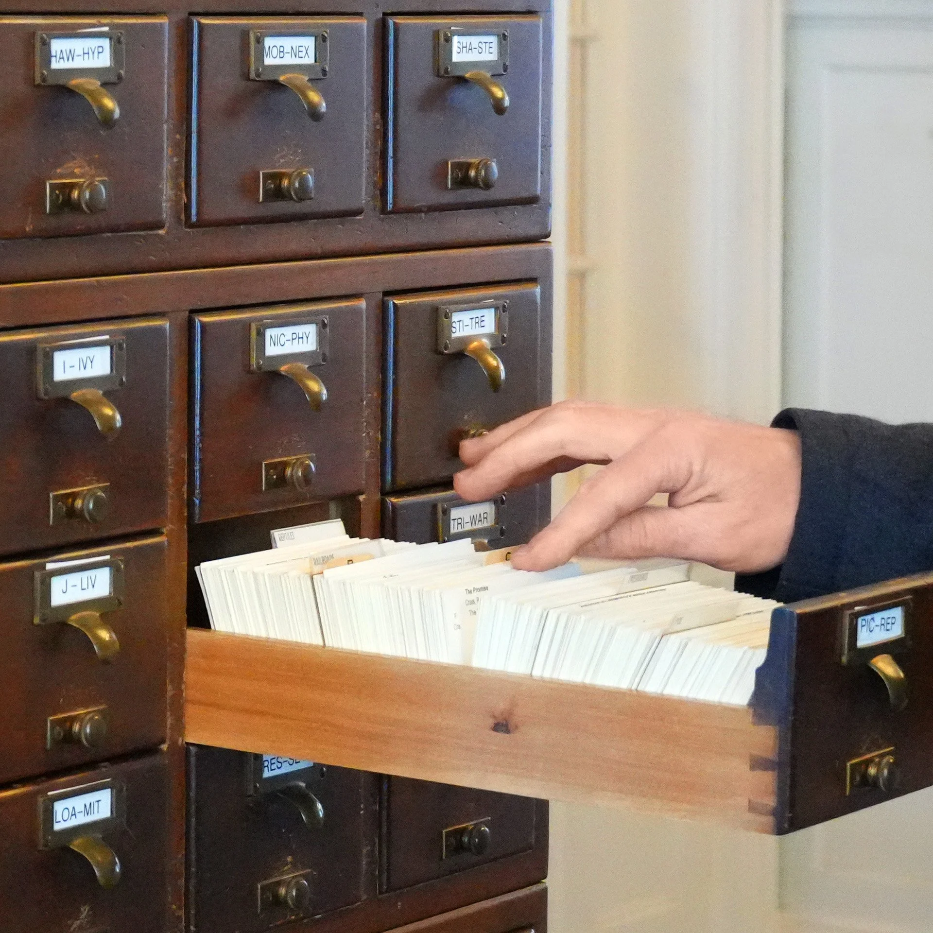 Close-up of a vintage wooden mailbox with multiple compartments, each labeled with different code names, with a person placing or retrieving mail.