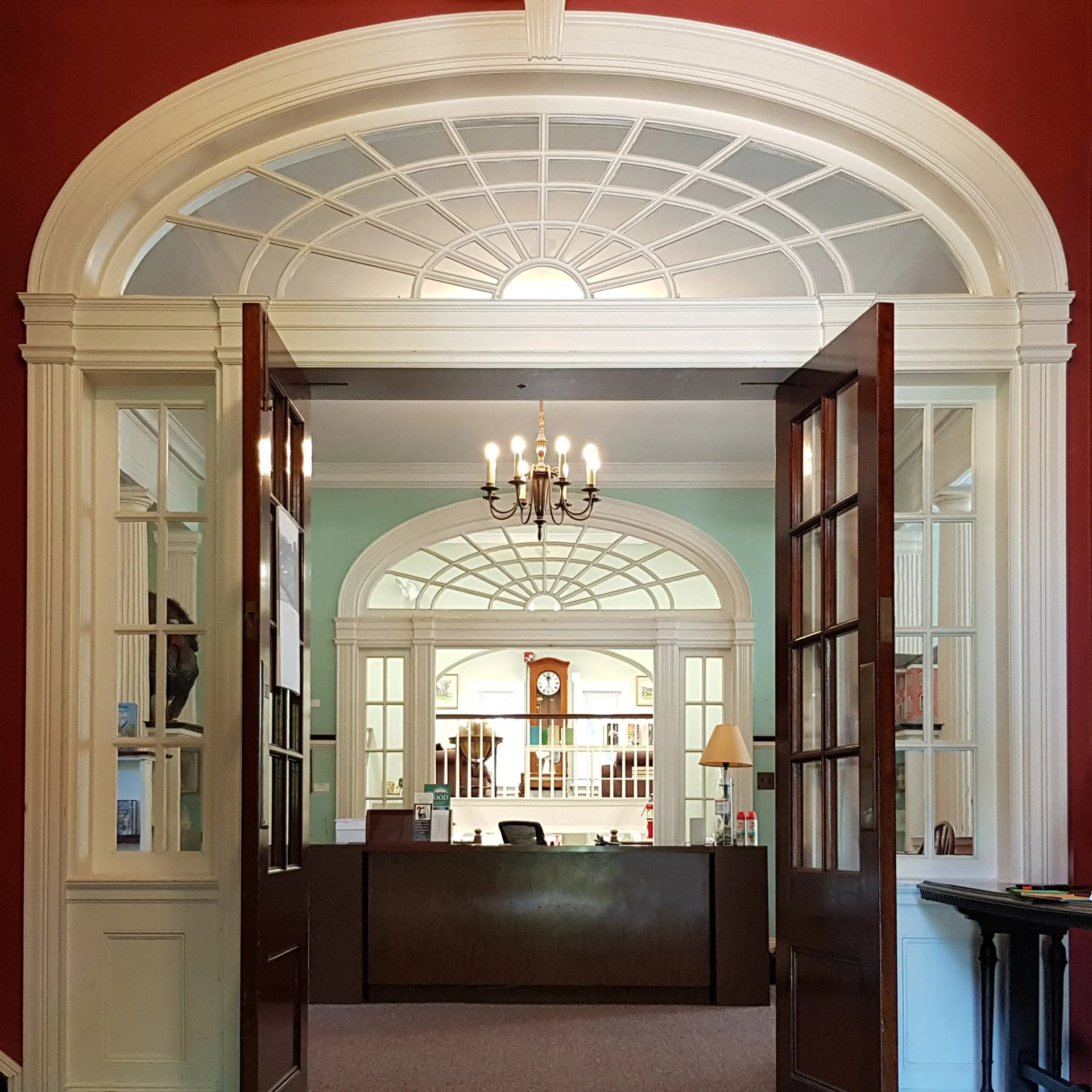 View through wooden and glass partition doors into a room with a large arched window, chandelier, and furniture.