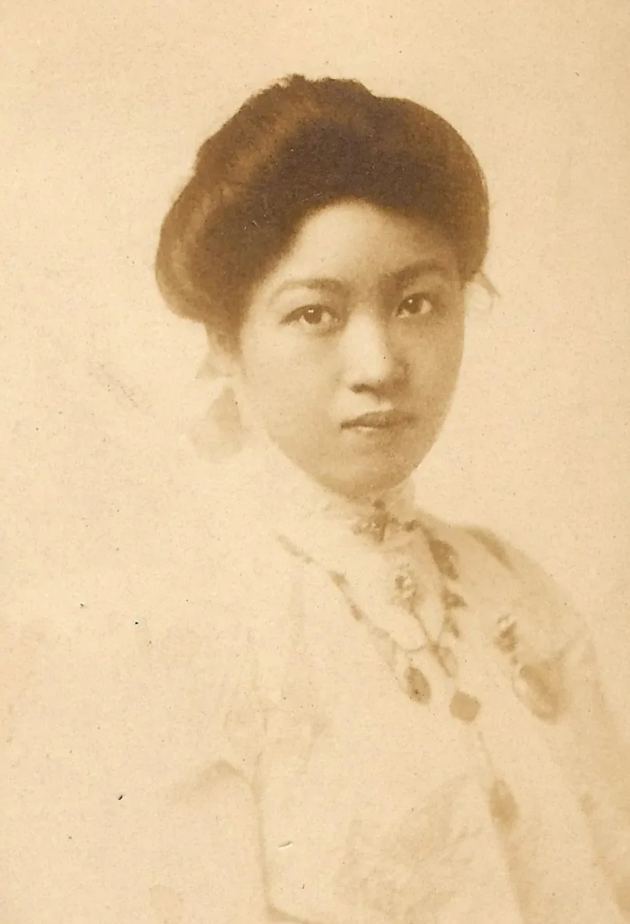 A sepia-toned vintage portrait of a woman with styled hair, wearing jewelry and a patterned dress.