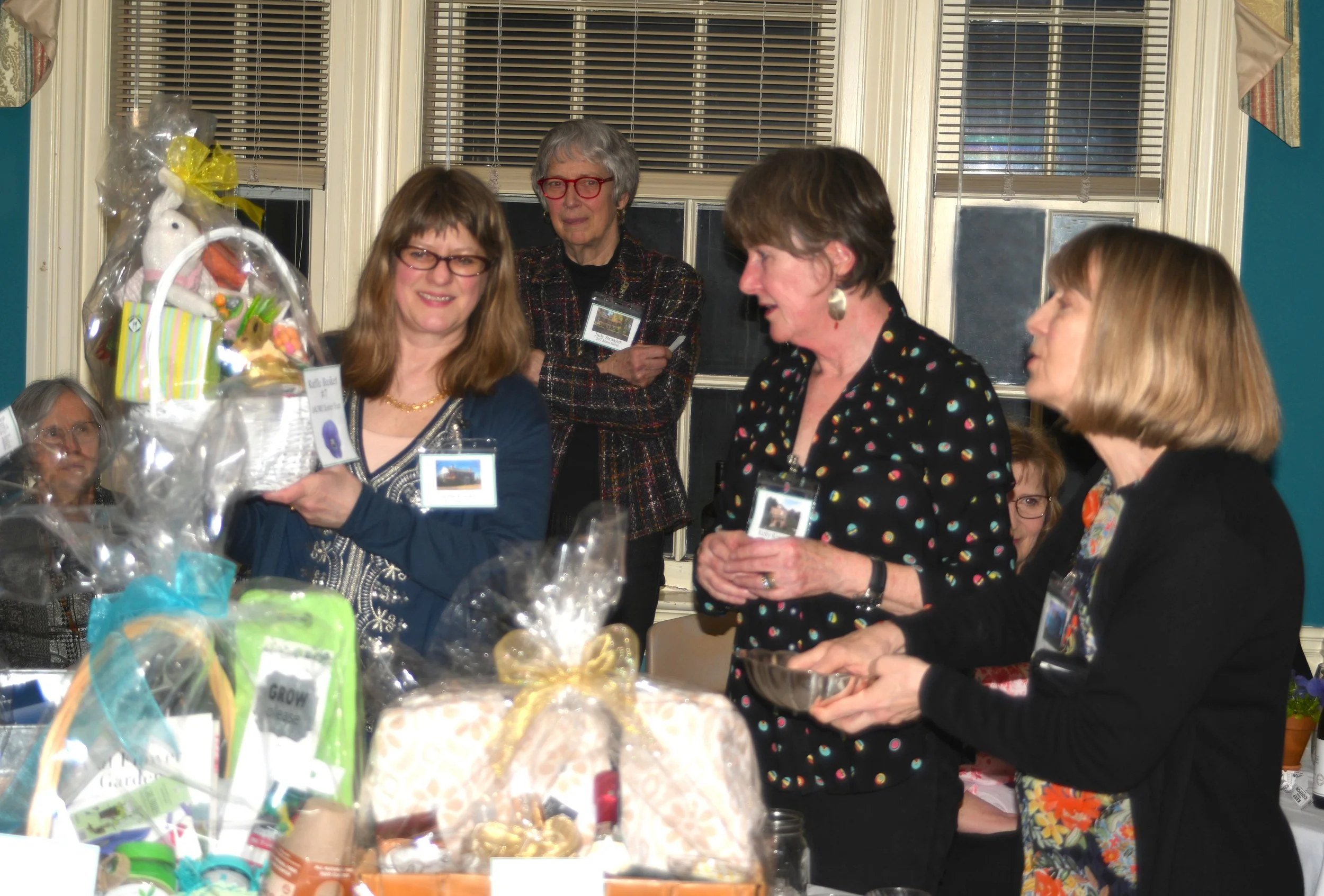 A group of four women gathered around a table with various decorated baked goods and wrapped gifts, engaging in conversation during a celebration or event.