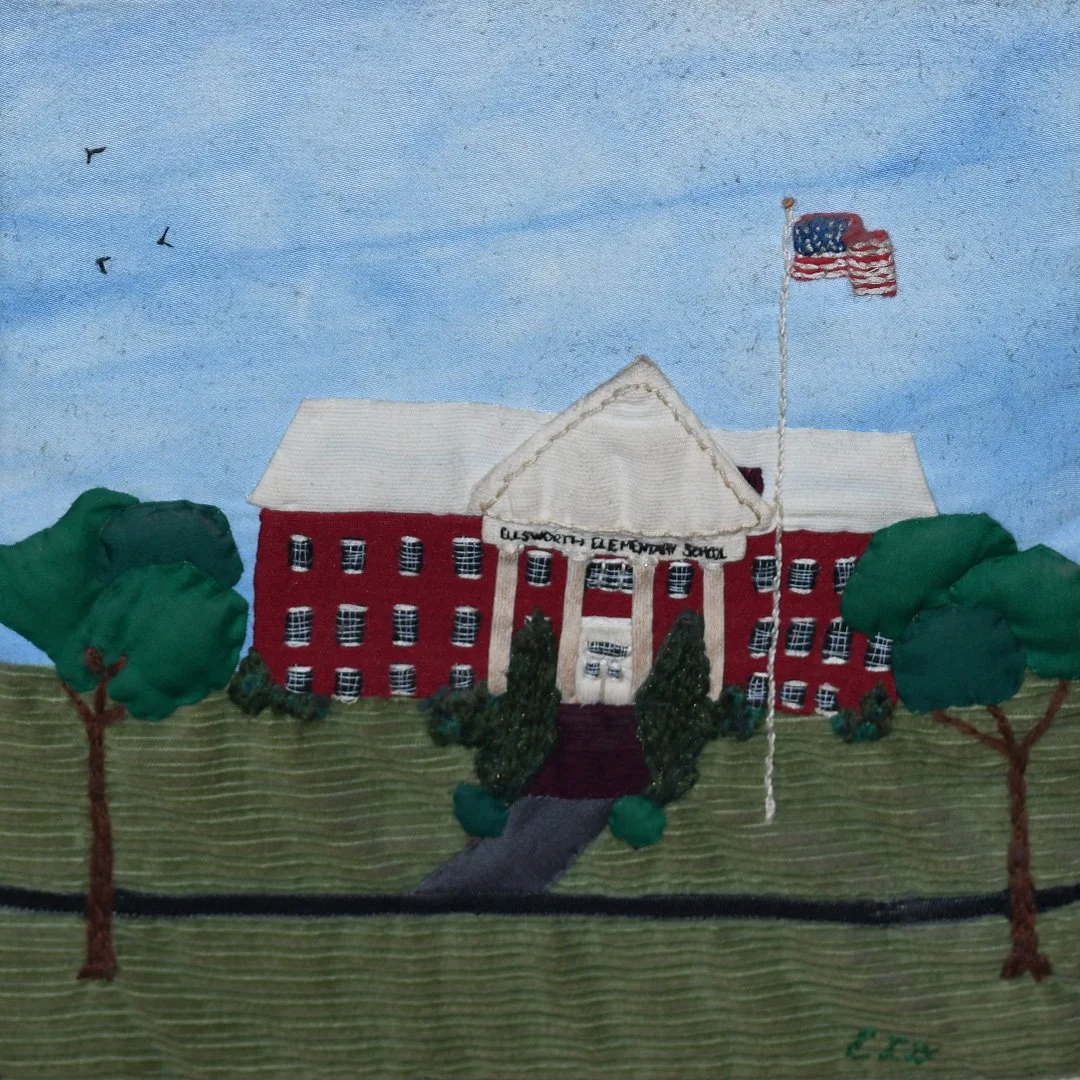 Embroidery of a red school building with trees, an American flag, and a blue sky with clouds and birds.