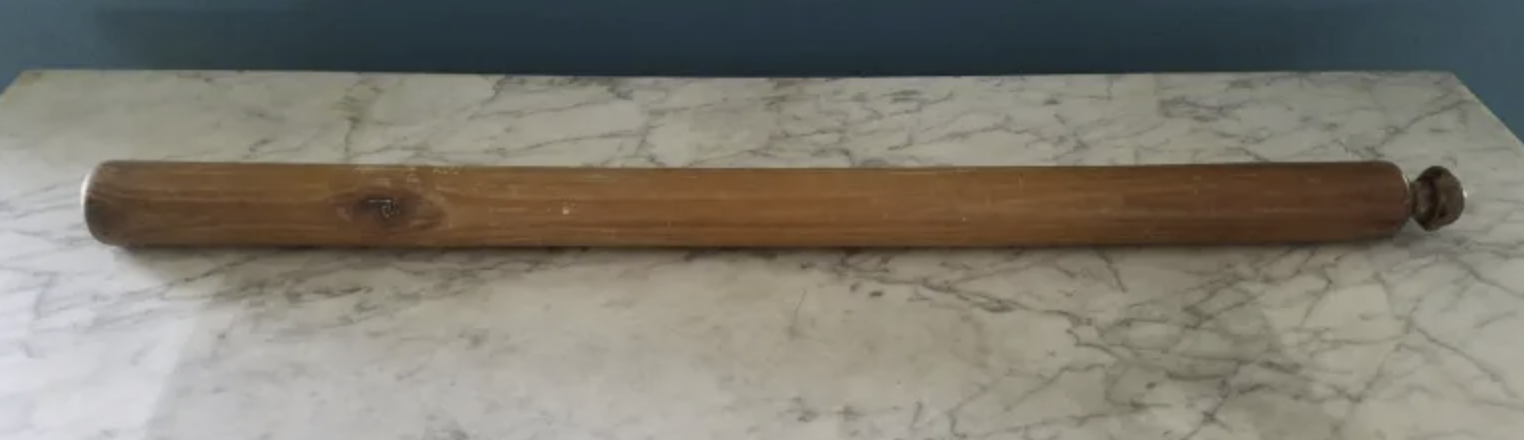 A wooden rolling pin resting on a marble countertop.