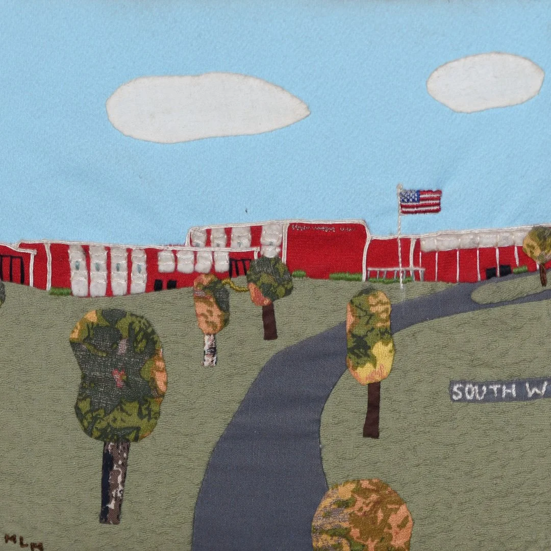Embroidery depicting a school building with red walls, an American flag, and trees on a grassy hill under a blue sky with clouds.