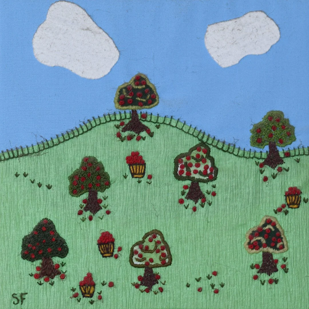 Embroidery of a green hill with multiple fruit trees, baskets of red apples, and a blue sky with two white clouds.