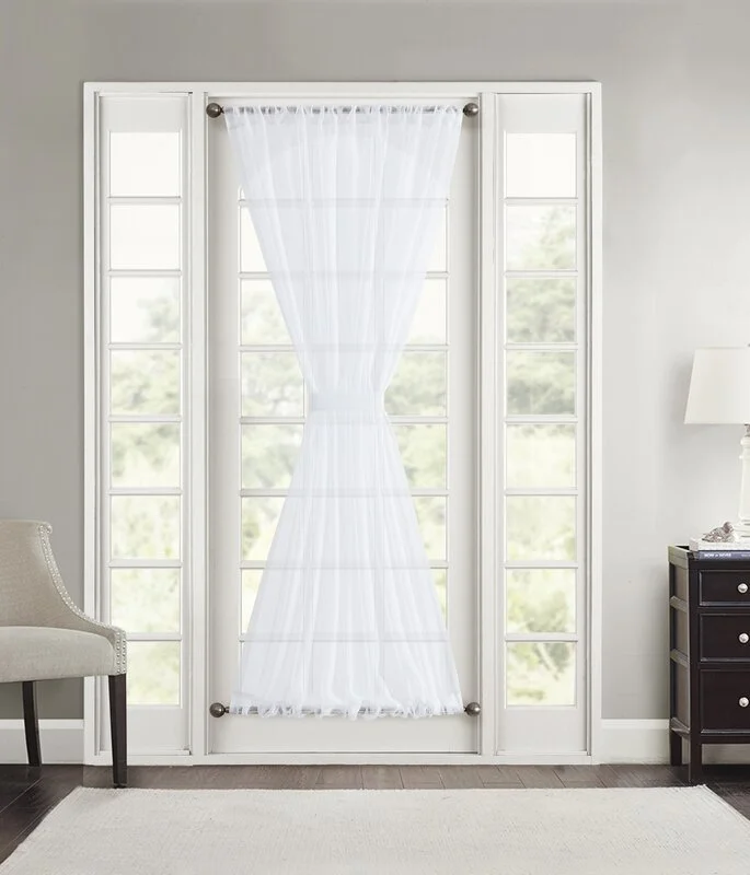 White sheer curtain on a French door with side windows, in a bright room with a chair on the left and a nightstand with a lamp on the right.