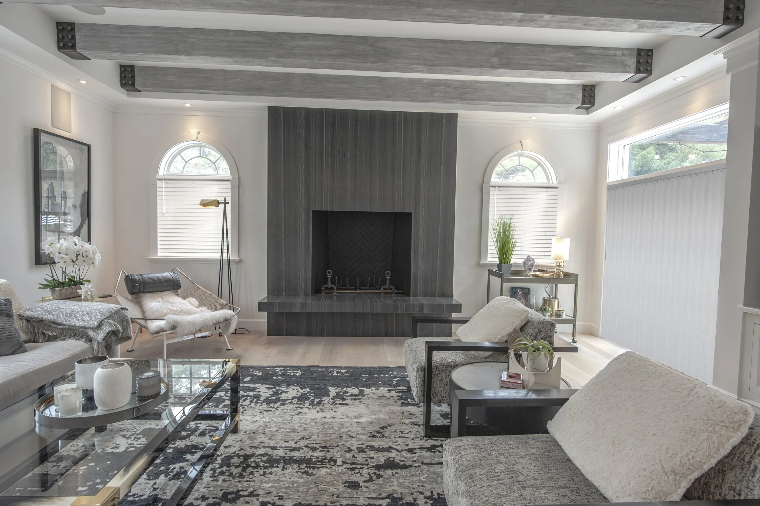 Living room with a fireplace, gray and cream furniture, large windows, and modern decor.