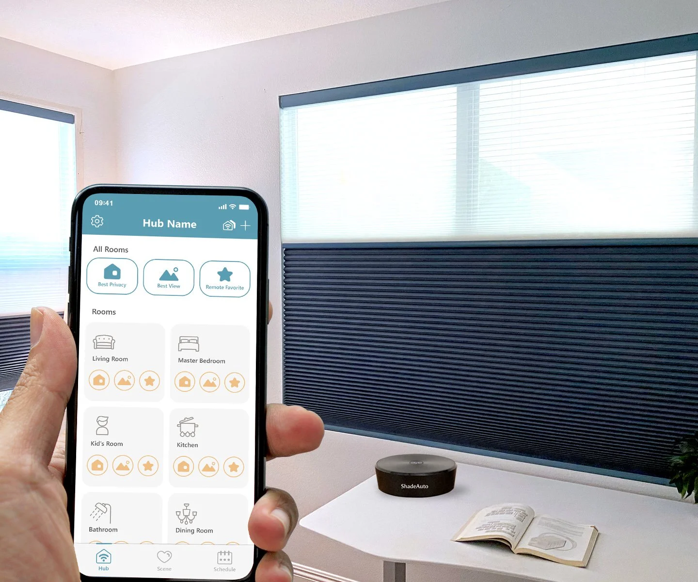 A person holding a smartphone with a smart home app visible, showing room controls, near a white desk with an open book, a circular black device labeled 'ShadeAuto,' and a small plant, in a room with white walls and windows.