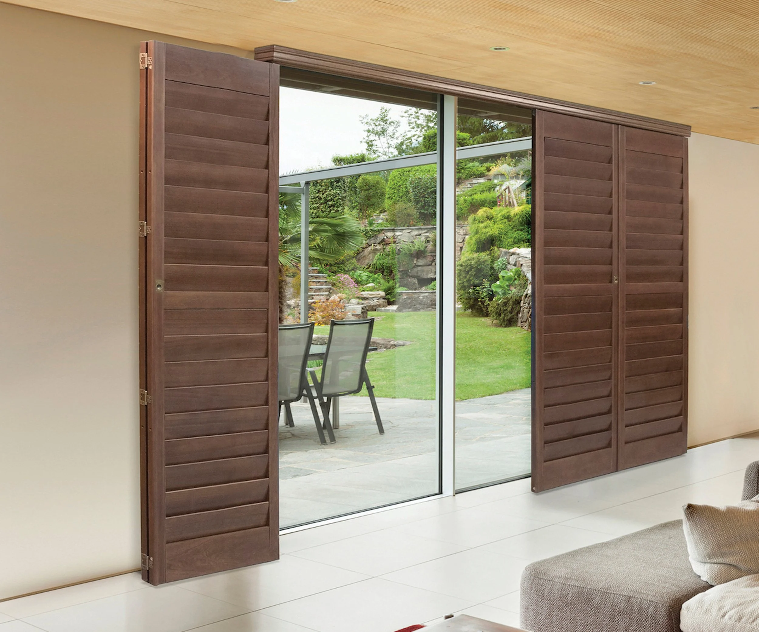 Sliding glass door with wooden shutters leading to a backyard with patio, chairs, lush green grass, stairs, and landscaped rock garden.