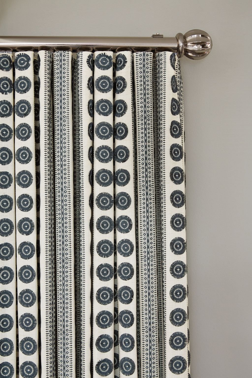 Black and white patterned curtain hanging from a metal curtain rod with a decorative finial, against a plain wall.