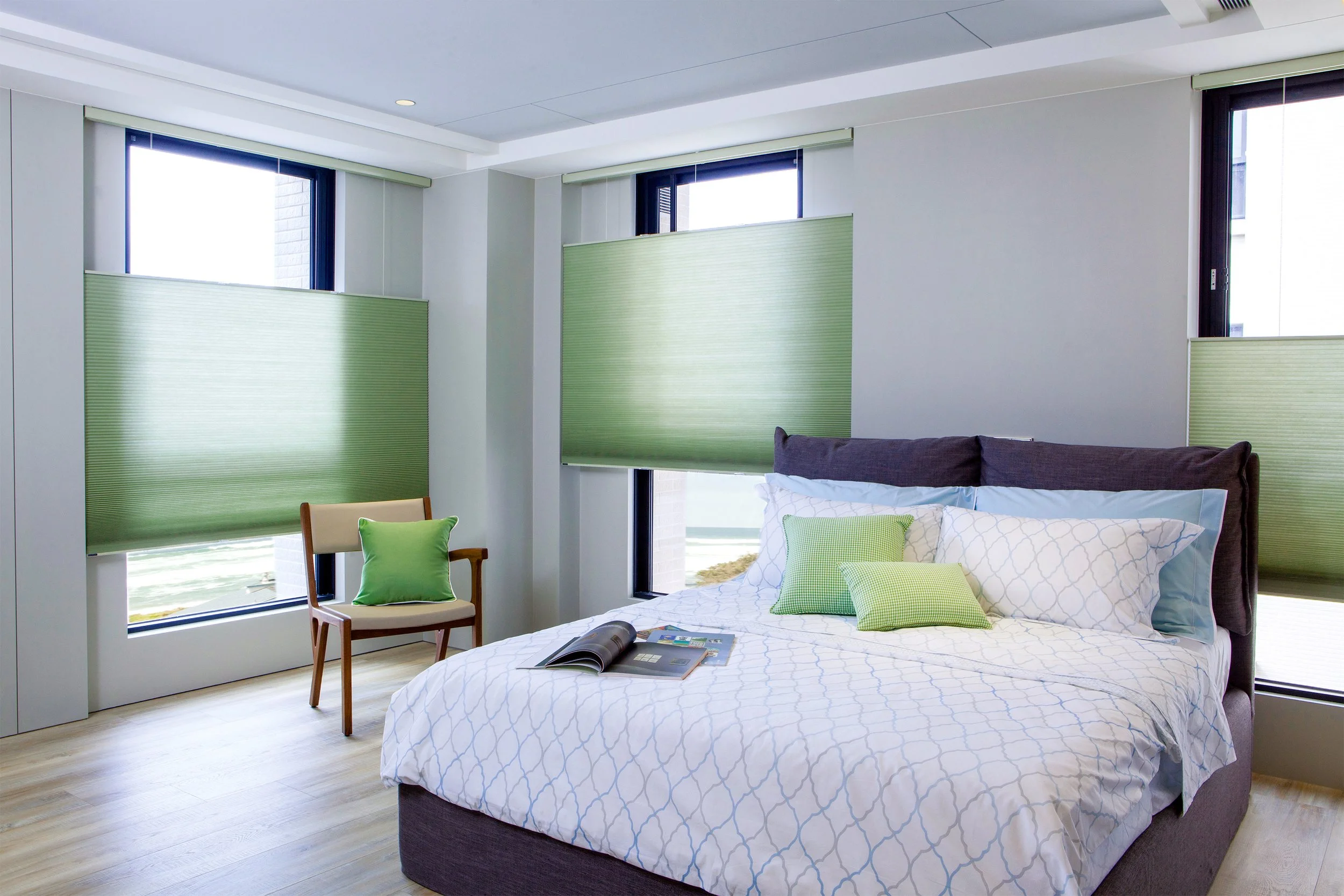 Modern bedroom with a bed, green pillows, and window shades.