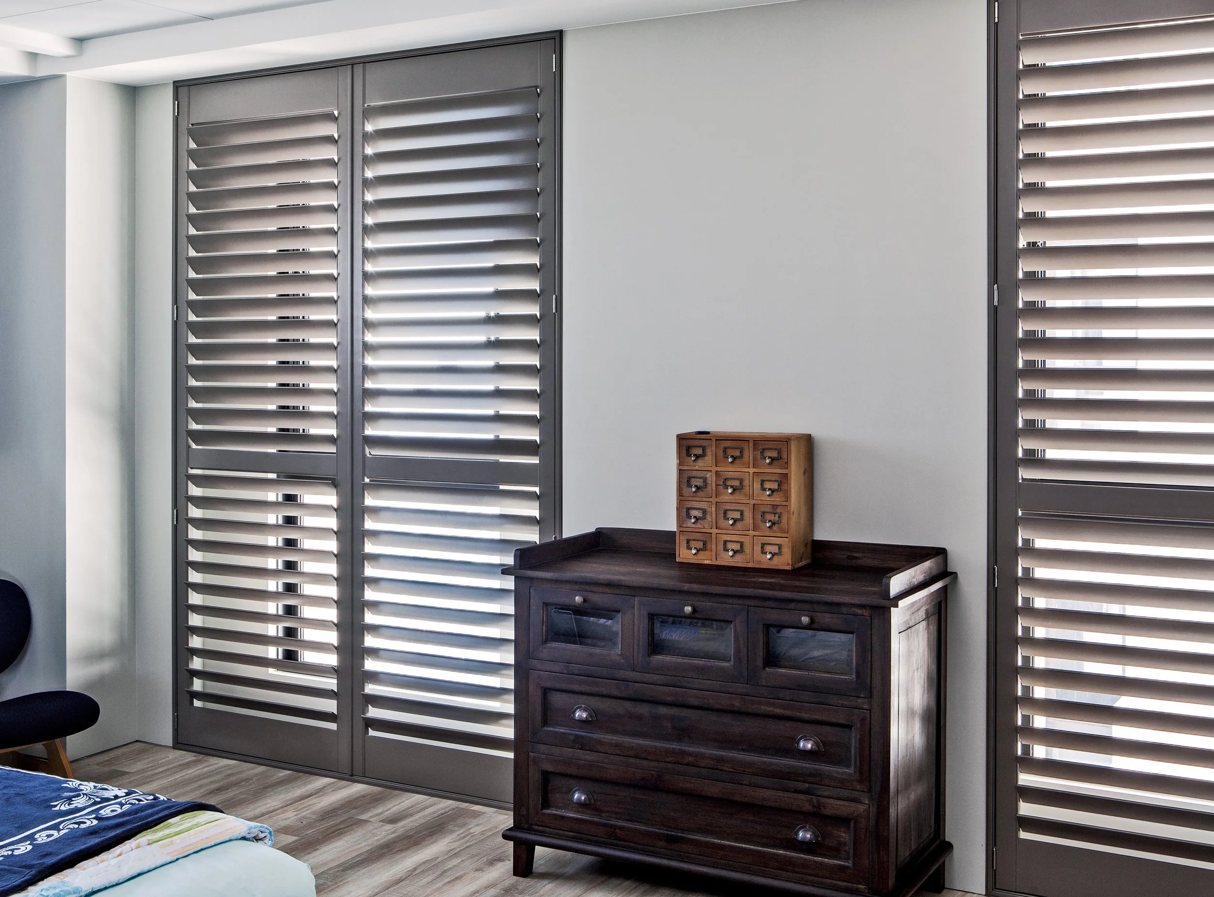 Interior of a room with gray window shutters, a dark wooden dresser, and a small wooden cabinet with multiple drawers on top.