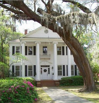 White two-story house with columns, front porch, and a large tree with hanging moss in the yard.