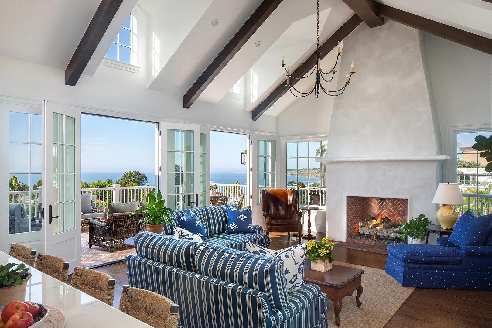 Living room with large windows, ocean view, fireplace, and wood ceiling beams.