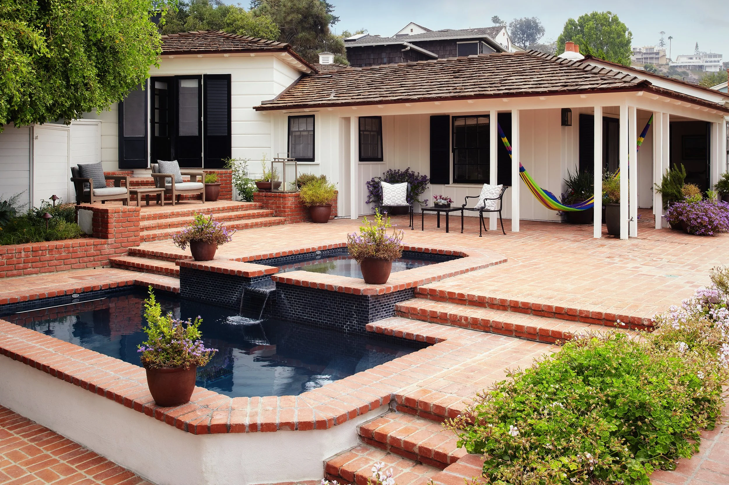 Backyard with brick patio, swimming pool, potted plants, outdoor seating, and a covered porch with chairs, a hammock, and potted plants.