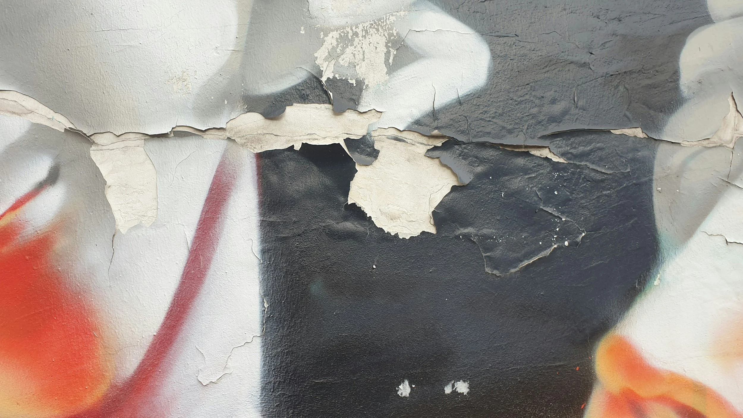 Close-up of a wall with peeling paint and graffiti, revealing multiple layers of paint underneath.