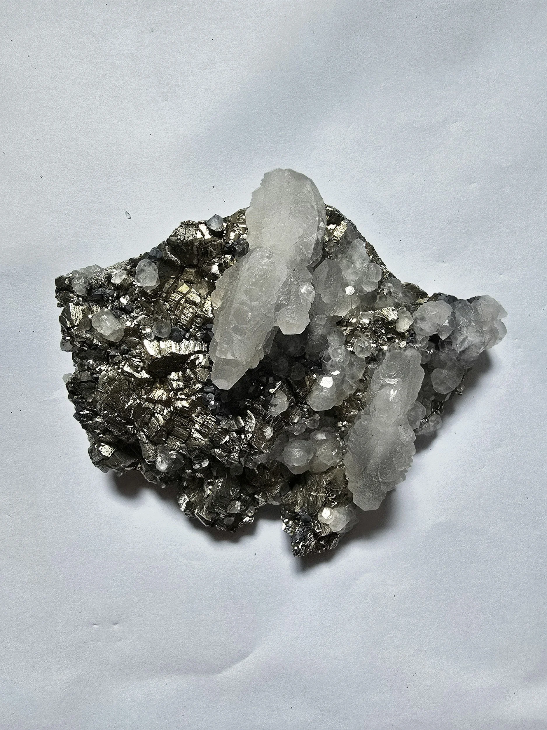 Close-up of a mineral rock specimen featuring metallic silver crystals with clear quartz or calcite formations on top.