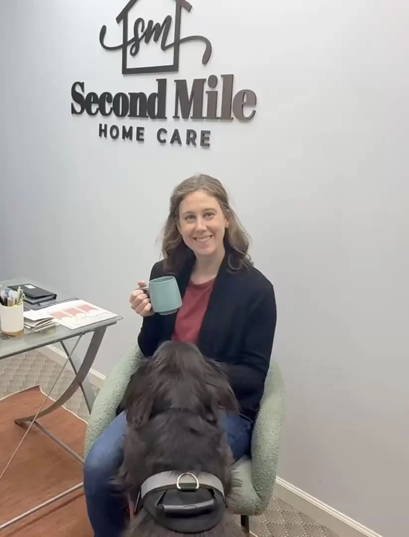 Second Mile Home Care Female owner with her black dog, holding cup of coffee in her office