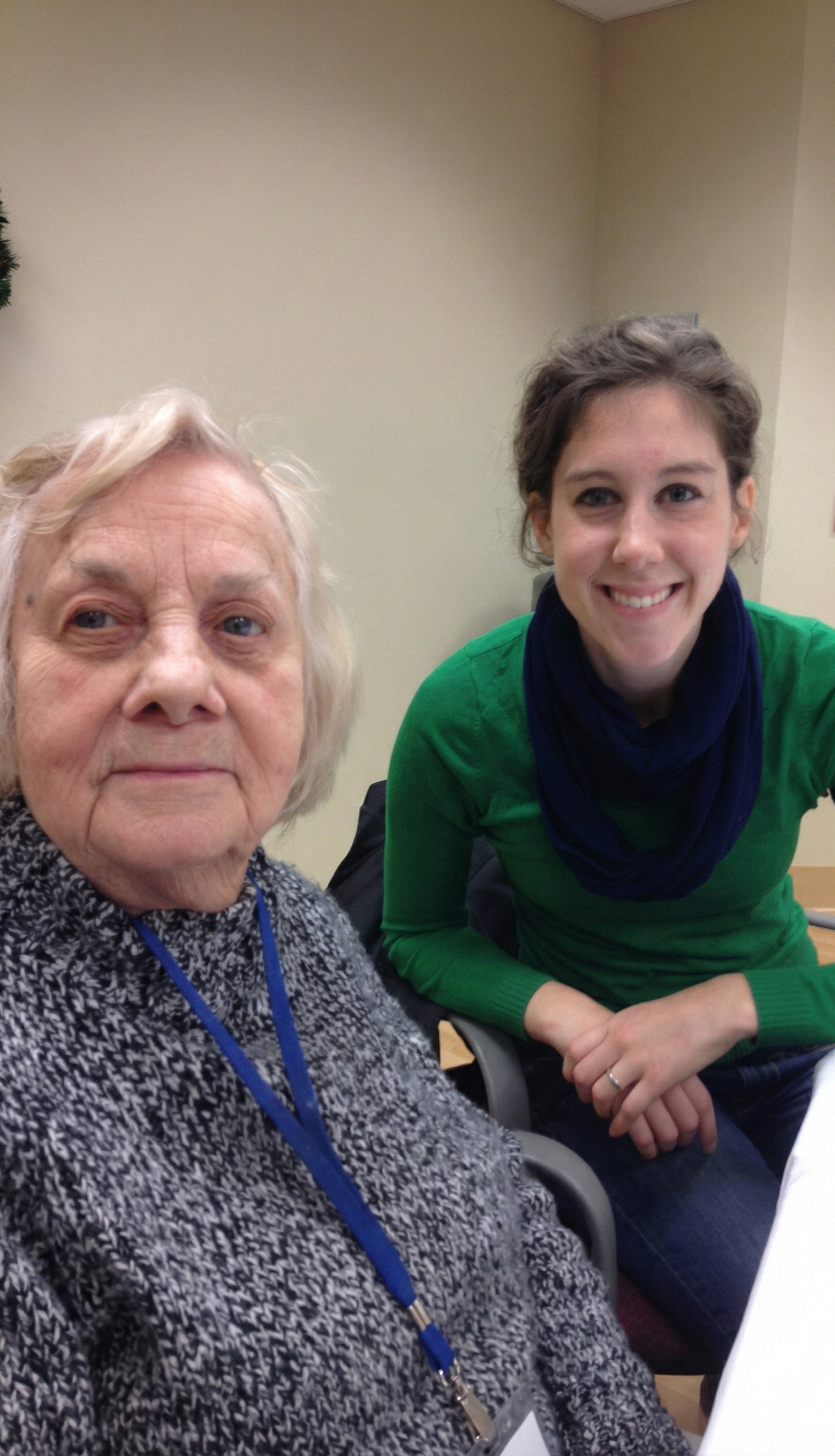 A photo of an elderly woman with gray hair and a young woman with dark hair, both smiling, sitting at a table in an indoor setting.