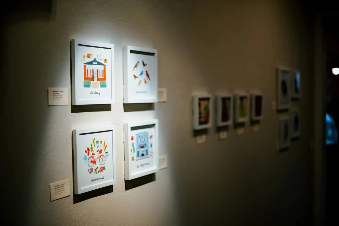 Art gallery wall with framed colorful illustrations and small description labels.