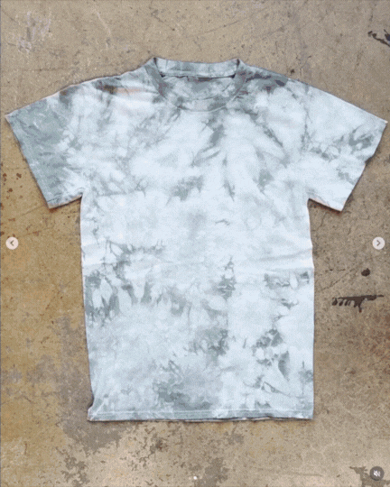 Gray and white tie-dye T-shirt lying flat on an outdoor concrete surface.