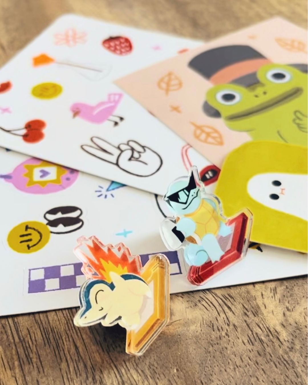 Colorful stickers and sheets of paper with cartoon characters and drawings, placed on a wooden surface.