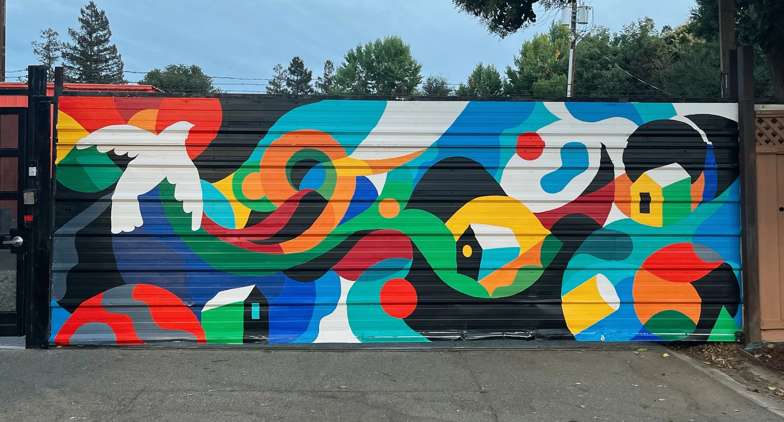 Colorful abstract geometric mural painted on a metal garage door, featuring circles, lines, triangles, and shapes in red, blue, green, yellow, black, orange, and white.
