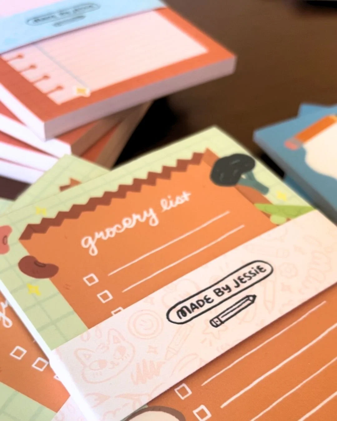Colorful printable grocery list notepad with checkboxes, made by Jessie, decorated with illustrations of food and kitchen items.