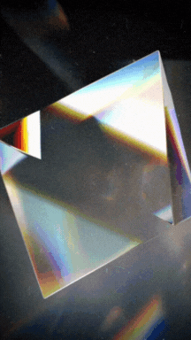 A clear rectangular prism of glass or crystal, reflecting and refracting light with rainbow colors, set against a dark background.
