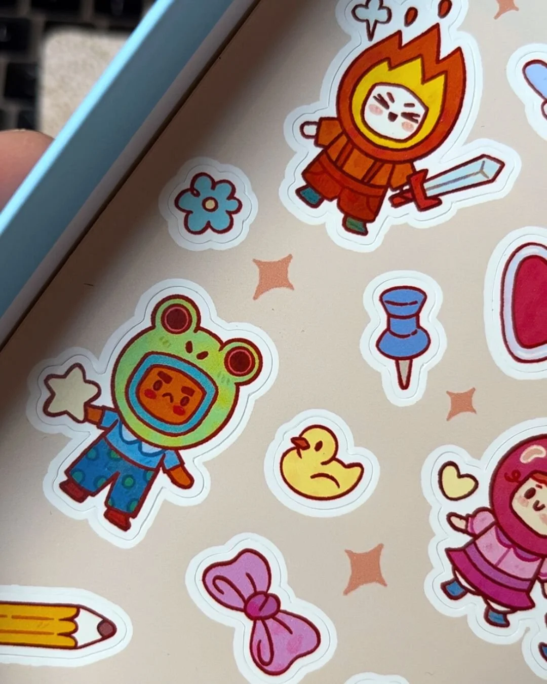 Collection of colorful cartoon stickers featuring characters in costumes, a rubber duck, a star, a flower, a bow, and small decorative shapes on a beige background.