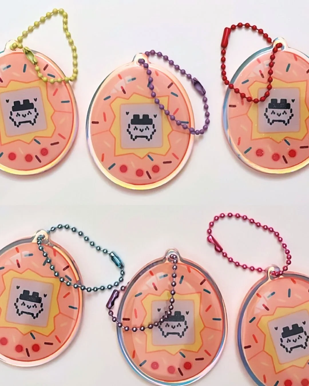 Six colorful Oreo keychains with cute pixel art faces and bead chains in gold, purple, red, blue, silver, and pink, placed on a white background.