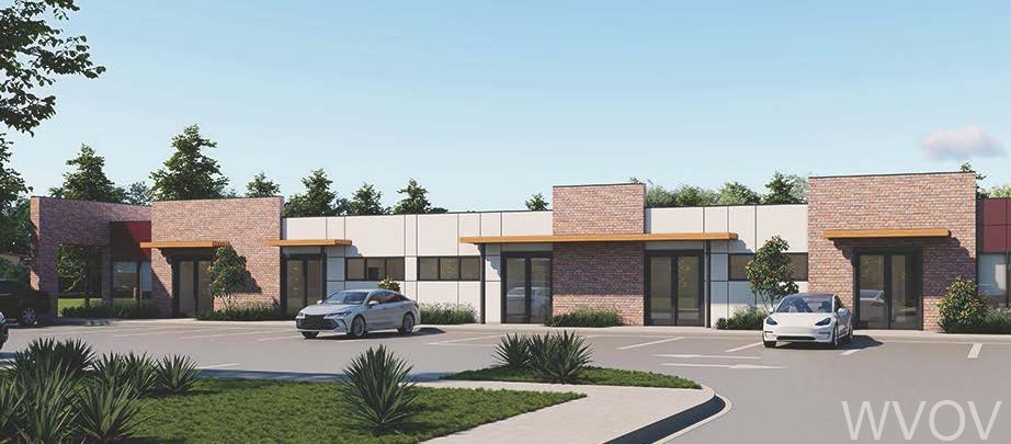 A modern commercial building with a brick and white exterior, parking lot with cars, and landscaped bushes and grass in the foreground.