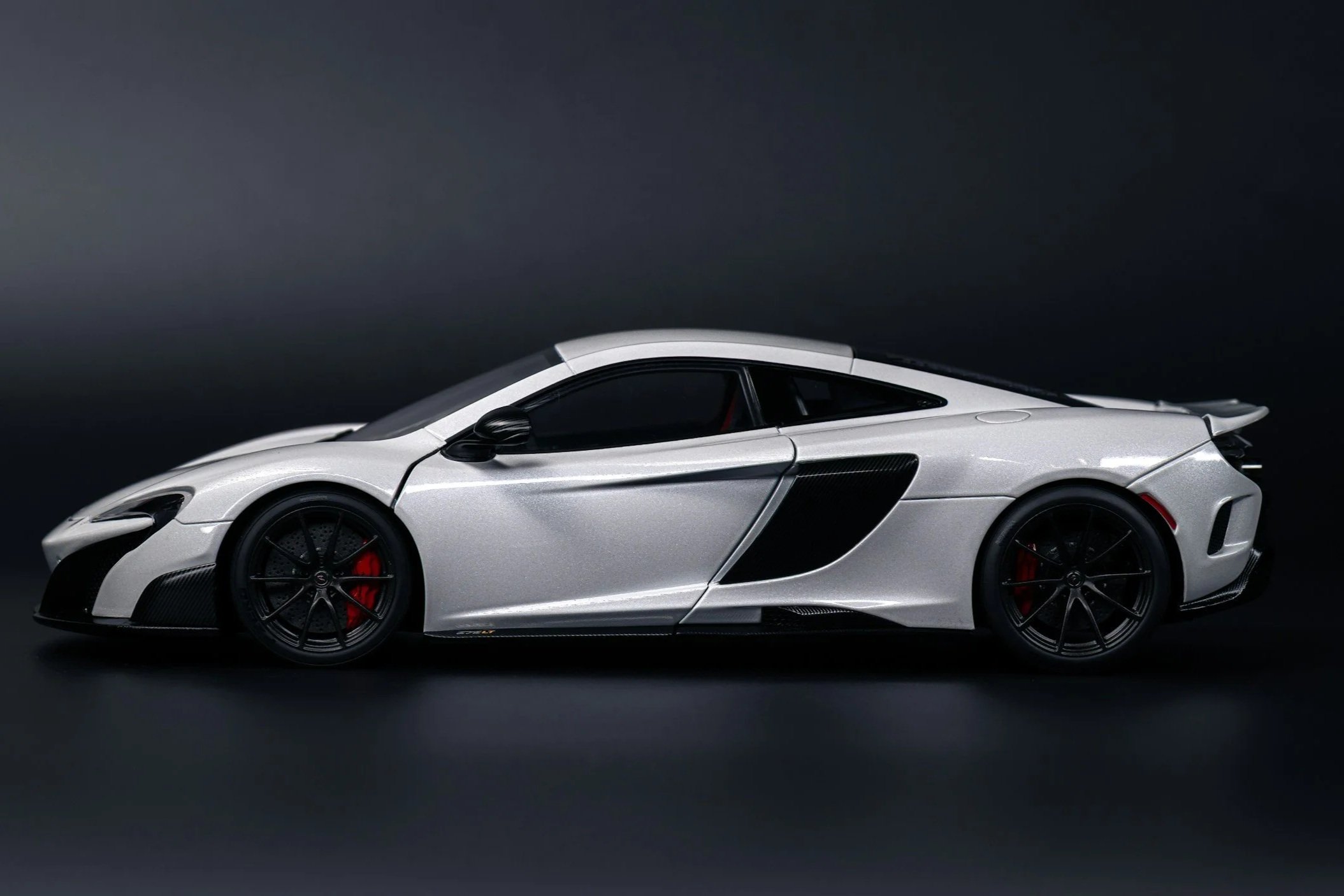Side view of a silver modern sports car with black wheels and red brake calipers, set against a dark background.