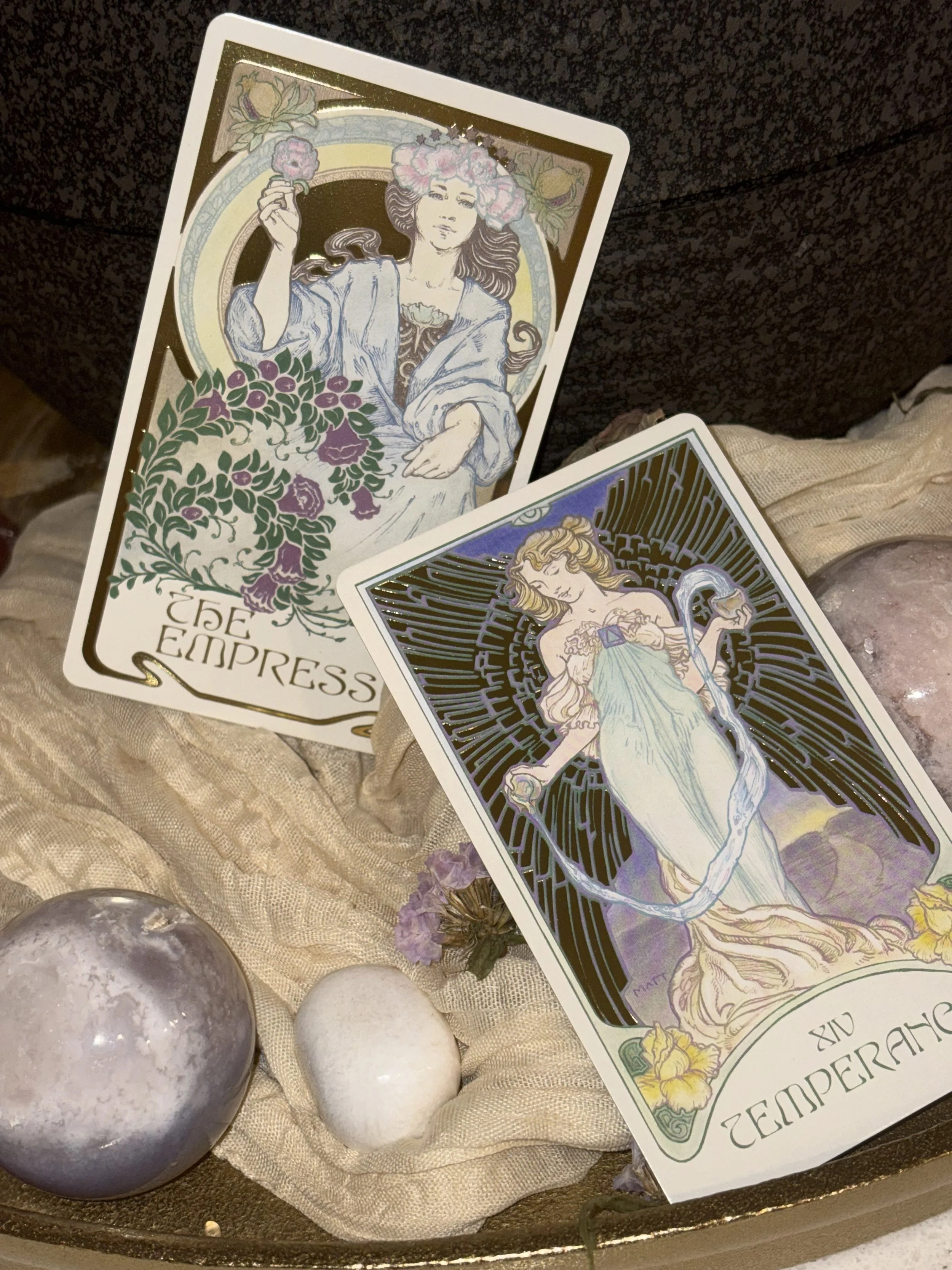 Two tarot cards, the Empress and the Emperess, are displayed on a textured fabric with decorative crystals and small flowers.