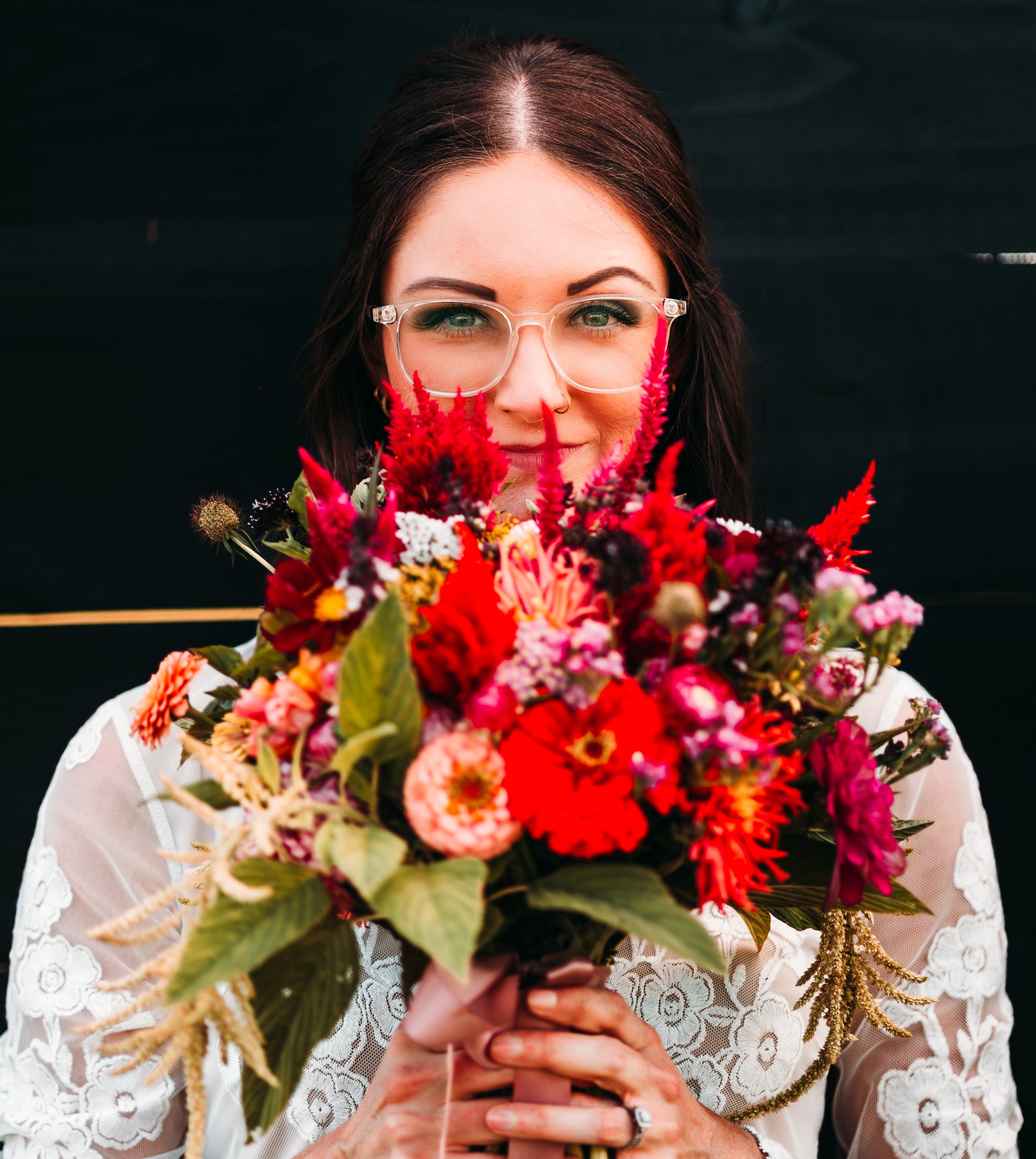 Woman with glasses holding a colorful bouquet of flowers in front of her face