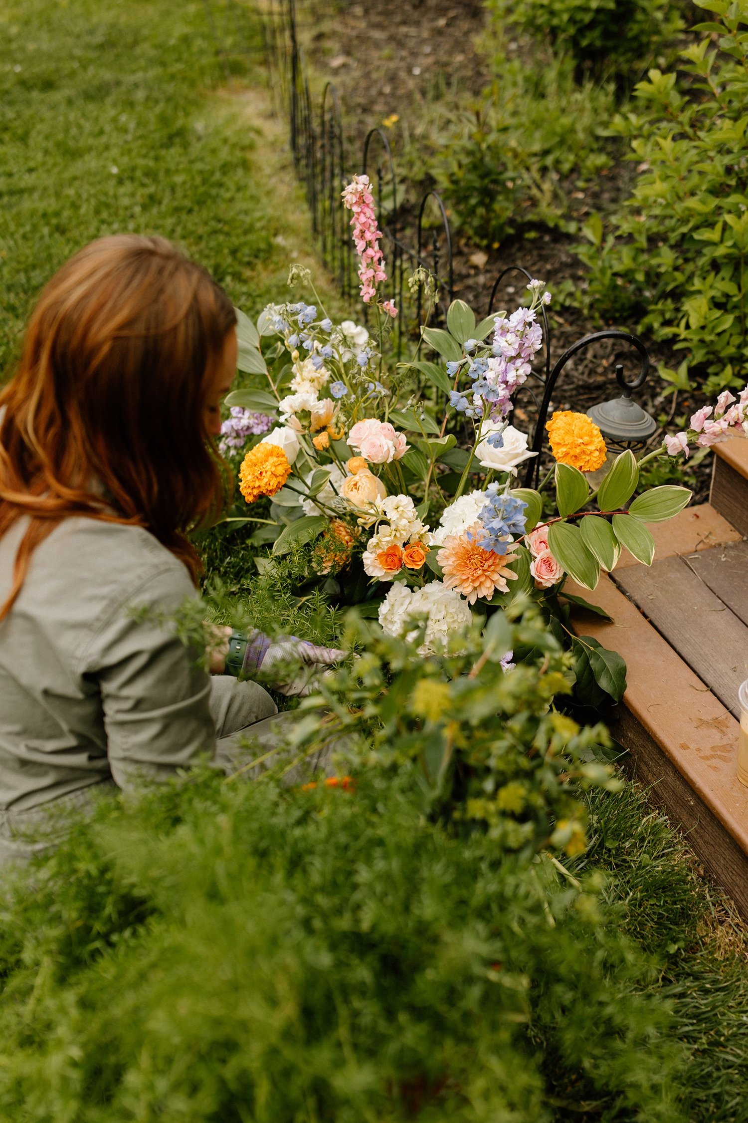 A woman tending to colorful flowers in a garden near stairs and a walkway.