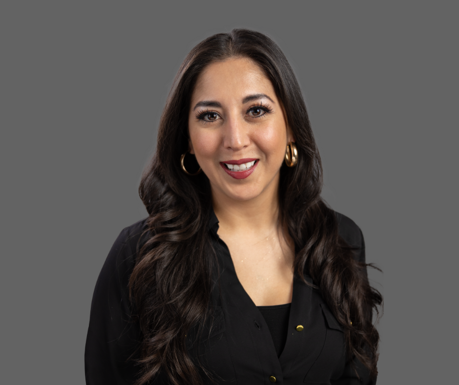 A woman with long dark hair, wearing gold hoop earrings and a black top, smiling against a gray background.