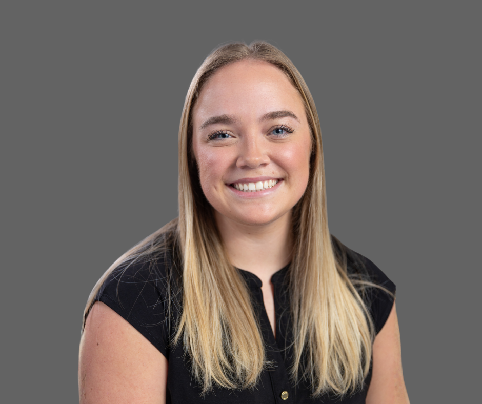 A young woman with long blonde hair, smiling and wearing a black top, against a gray background.