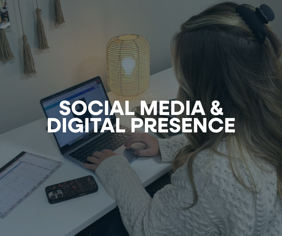 A woman with long hair in a bun working on a laptop at a white desk, surrounded by a smartphone, planner, and a lit paper lantern