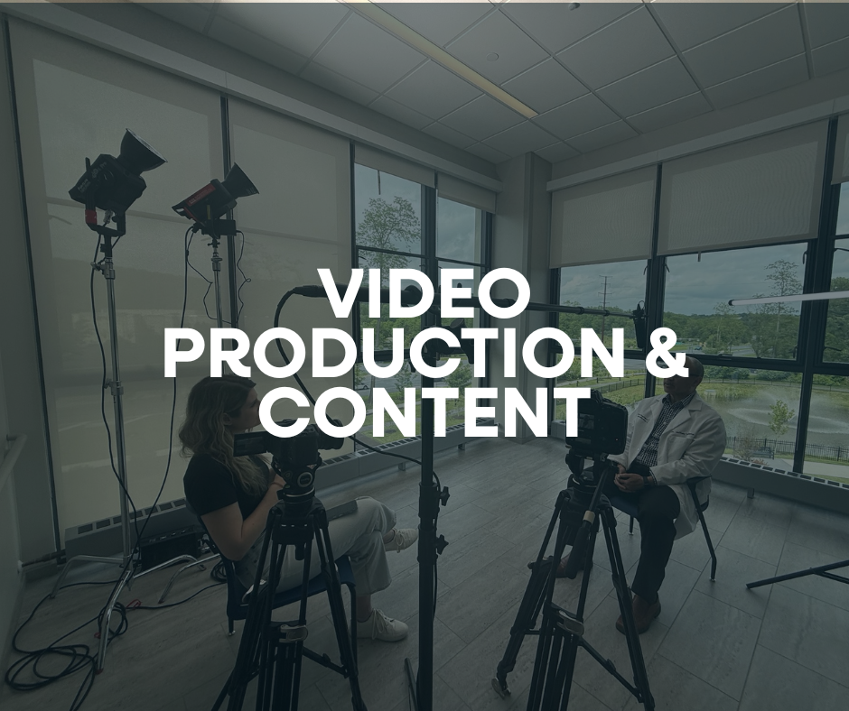 Inside a modern room with large windows showing trees and a cloudy sky, two people are filming a video with professional cameras and lighting equipment. The overlay text reads 'Video Production & Content'.