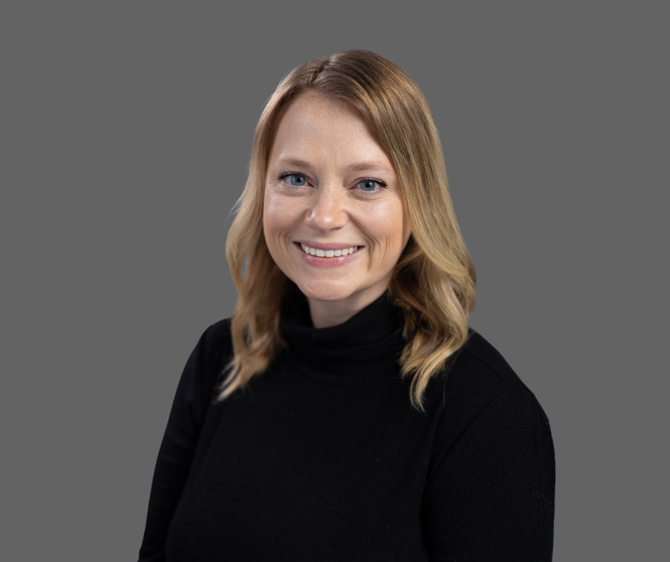 A woman with shoulder-length blonde hair, blue eyes, smiling, wearing a black turtleneck, against a gray background.