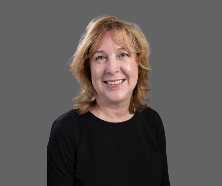 A smiling middle-aged woman with shoulder-length blonde hair, wearing a black top, against a gray background.