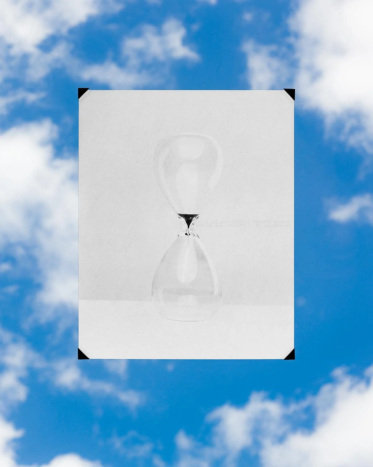 A black and white illustration of an hourglass with sand flowing from the top chamber to the bottom, set against a background of a partly cloudy blue sky.