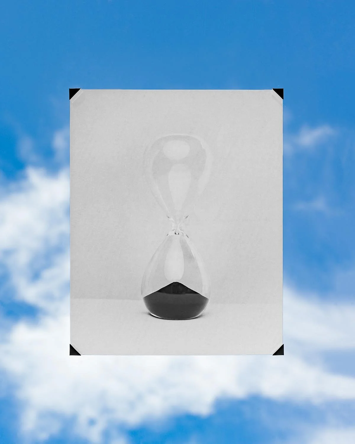 A photograph of a beach ball shaped like an hourglass with a glass top and bottom, containing sand, against a sky with clouds.